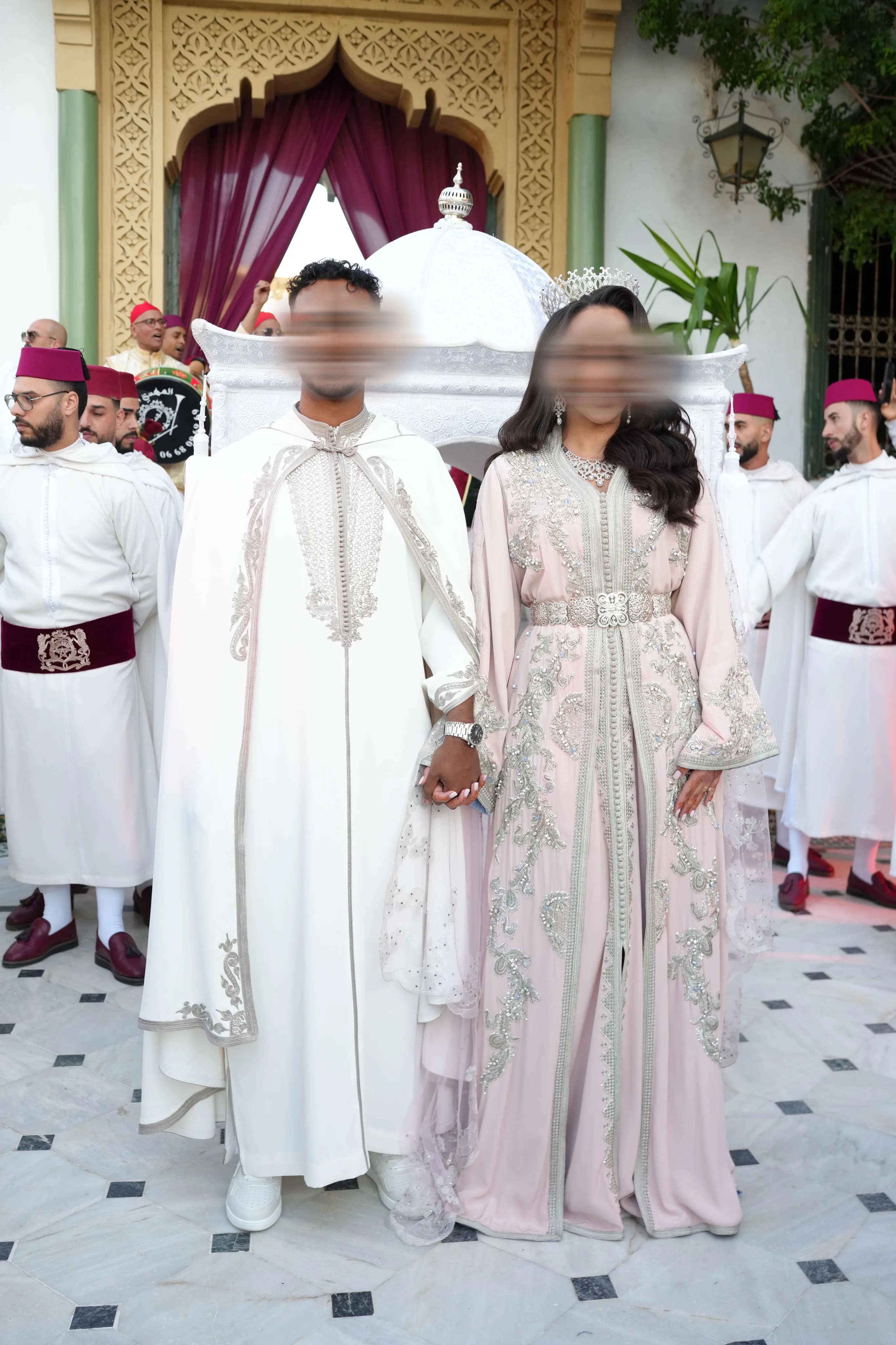 Couple de mariés en tenue marocaine, selham blanc brodé d'argent et caftan rose poudré