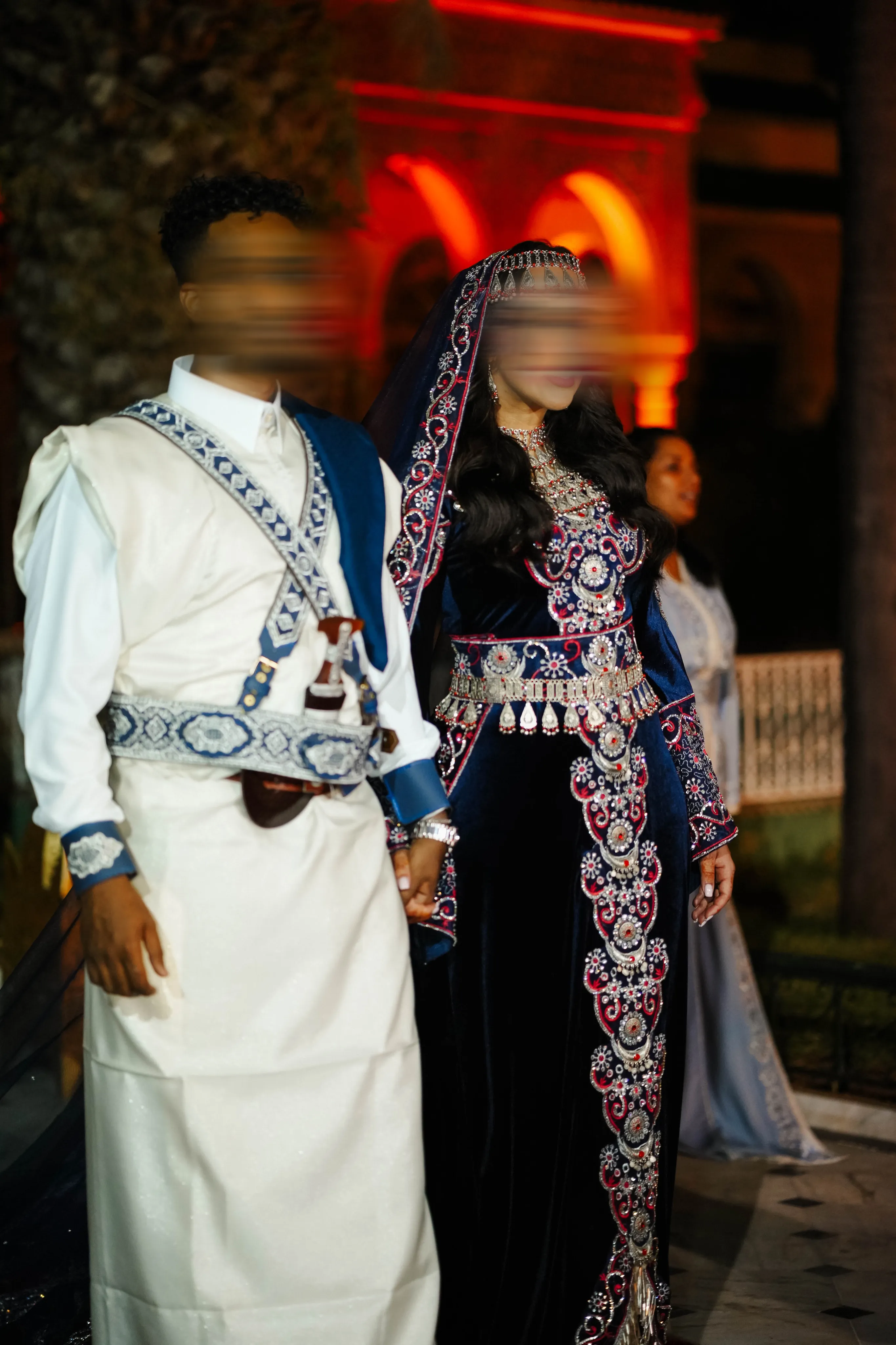Couple de mariés en tenue yéménite : mariée en velours bleu nuit brodé d'argent, marié en thobe blanc à baldric